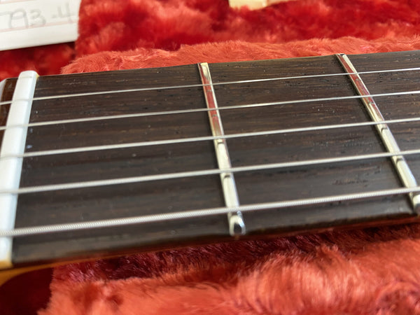 Close-up of acoustic guitar fretboard showing steel strings and metal frets on wooden neck with white nut on red plush background