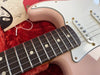 Close-up of rosewood fingerboard and strings on pink electric guitar with white pickguard in red plush case