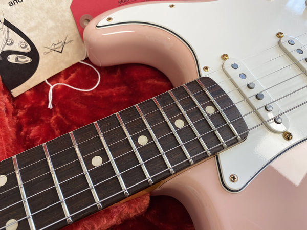 Close-up of rosewood fingerboard and strings on pink electric guitar with white pickguard in red plush case