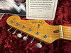 Close-up of vintage Fender Stratocaster guitar headstock with six tuning machines, original bone nut, and strings in red plush hardshell case with certificate of authenticity