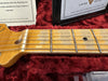 Close-up of vintage maple guitar neck and fretboard with metal frets and dot inlays on red plush guitar case lining with certificate of authenticity from Fender Custom Shop Corona California