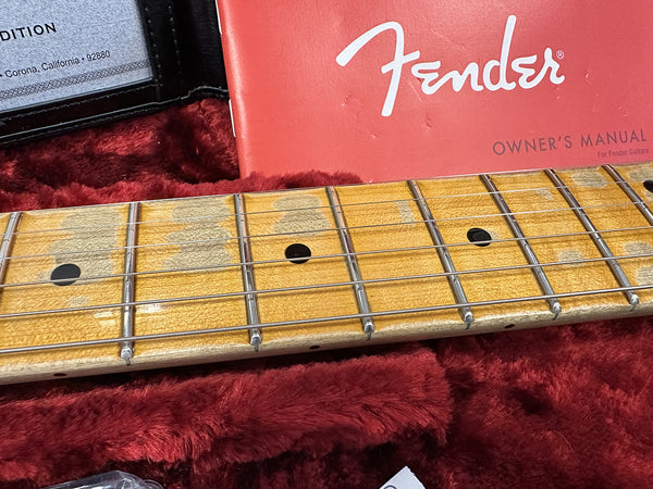 Close-up of worn maple guitar fretboard with black dot inlays and Fender owner's manual on red plush guitar case lining