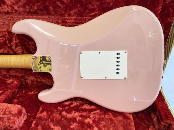 Back view of a pink solid body electric guitar with a white plastic back plate, maple neck, and gold neck plate on a red plush case interior