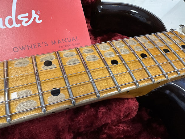 Close-up of worn maple fretboard on Fender electric guitar with Fender owner's manual and plush red guitar case interior