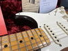 Close-up of white electric guitar fingerboard and pickups with vintage maple fretboard and detailed strings, displayed with guitar setup instructions and warranty booklet on plush red background.