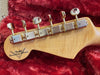 Close-up of Fender Custom Shop electric guitar maple headstock with six vintage-style tuning pegs on red plush guitar case lining