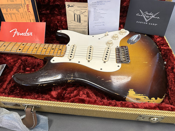Vintage Fender Stratocaster electric guitar in sunburst finish with wear and relic details, displayed in tweed case with red plush interior, Fender owner's manual, tremolo springs diagram, and Fender Custom Care documentation.