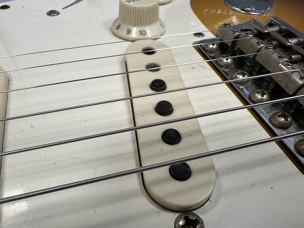 Close-up of electric guitar strings, white single-coil pickup, and tone knob on a vintage-style guitar body