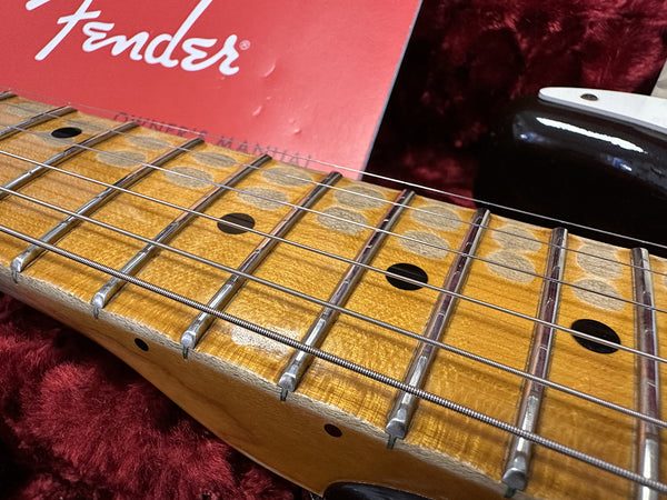 Close-up of Fender guitar maple neck and fretboard showing frets and strings with original Fender owner's manual in red background