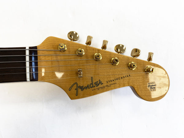Close-up of Fender Stratocaster guitar headstock with gold tuning pegs and rosewood fretboard on white background