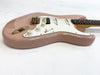 Pink electric guitar with white pickguard and gold hardware lying on white surface, close-up of body and control knobs