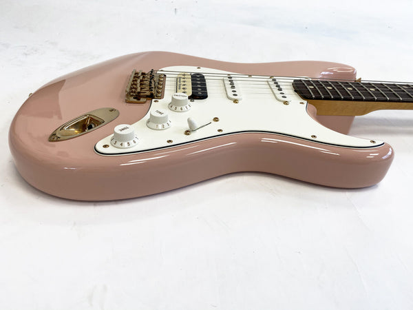 Pink electric guitar with white pickguard and gold hardware lying on white surface, close-up of body and control knobs
