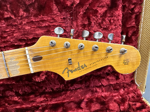 Close-up of vintage Fender Stratocaster guitar headstock with original contour body decal, six tuning pegs, and strings, shown inside red plush guitar case.