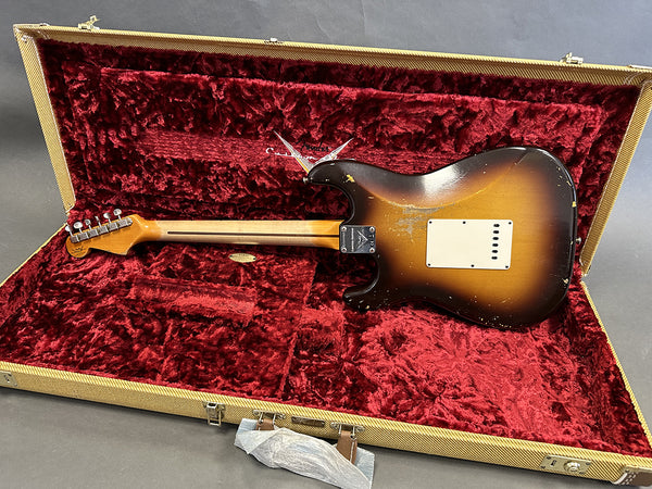 Vintage sunburst Fender Stratocaster electric guitar showing the back and neck inside an open red plush lined tweed hardshell case on gray background