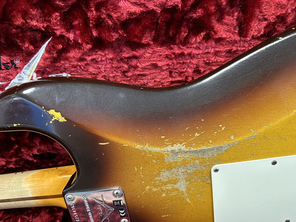 Close-up of vintage sunburst electric guitar body showing worn and chipped paint finish with metal neck plate and red plush guitar case lining in background
