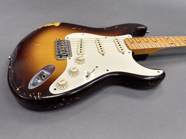 Vintage sunburst electric guitar with three single-coil pickups and maple neck on gray background, worn finish with visible chips and scratches