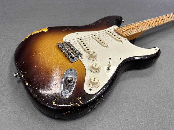 Vintage sunburst electric guitar with worn finish, three single-coil pickups, white pickguard, and maple neck on gray background