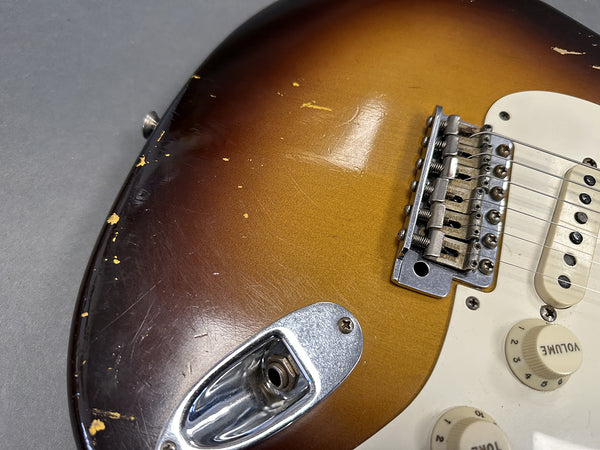 Close-up of sunburst electric guitar body showing vintage wear, metal output jack plate, bridge, pickups, and volume and tone control knobs