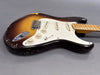 Vintage sunburst electric guitar body with white pickguard and three single-coil pickups, showing worn finish and aged maple neck on gray background