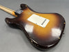 Back view of vintage sunburst electric guitar with worn finish and white plastic tremolo cover plate on gray background