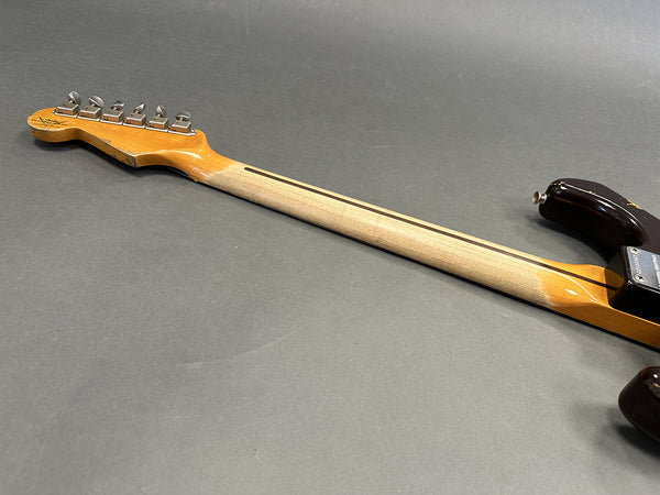 Vintage electric guitar neck with six tuning pegs, maple wood fretless neck with skunk stripe, and part of a worn dark finished guitar body on gray background.