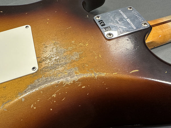 Close-up of worn sunburst finish on the back of a Fender Custom Shop electric guitar body with neck plate and screws visible.