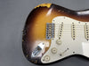 Close-up of vintage sunburst electric guitar body with worn finish, white pickguard, three single-coil pickups, and volume and tone control knobs.
