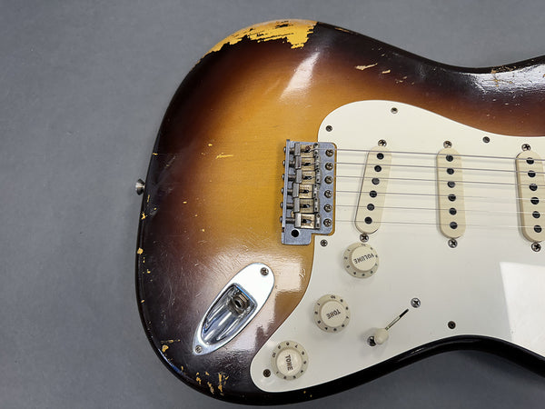 Close-up of vintage sunburst electric guitar body with worn finish, white pickguard, three single-coil pickups, and volume and tone control knobs.