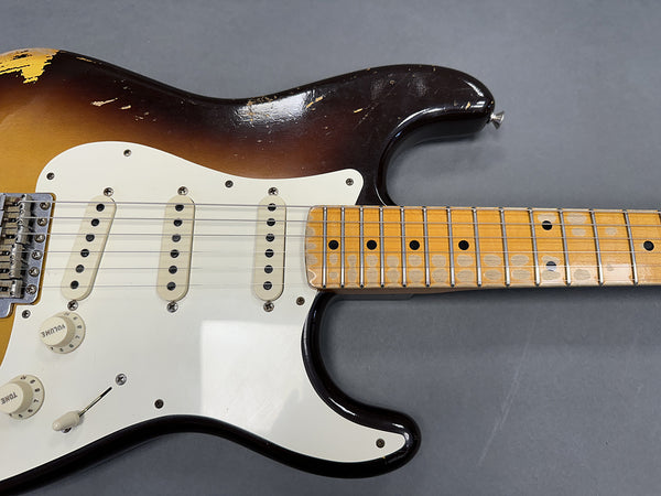 Close-up of vintage sunburst electric guitar body and maple neck with worn frets and white pickguard, showing volume and tone knobs on gray background.