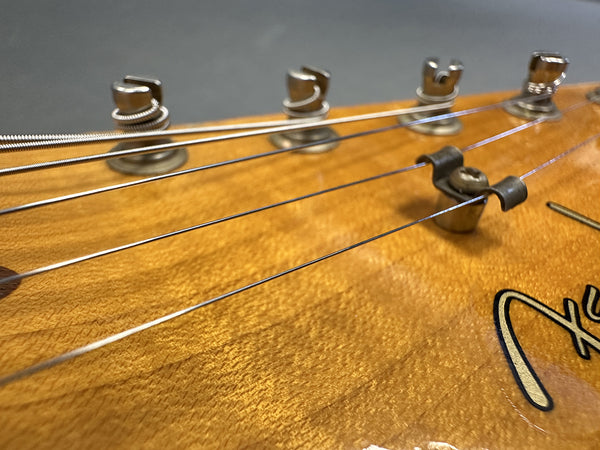 Close-up of natural wood guitar headstock with tuning pegs and metal strings winding around them at Coffee House Guitars