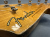 Close-up of worn Fender Stratocaster guitar headstock with vintage tuning pegs and visible Fender logo and string tree.