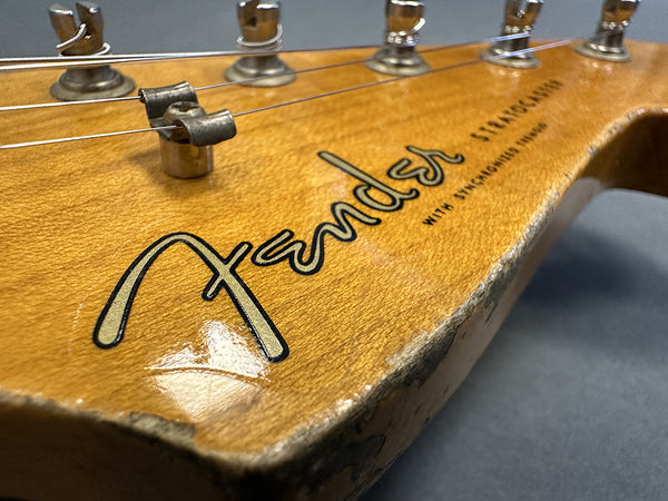 Close-up of worn Fender Stratocaster guitar headstock with vintage tuning pegs and visible Fender logo and string tree.