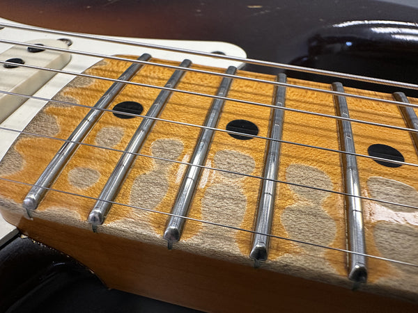 Close-up of worn maple fretboard with metal frets and black dot inlays on electric guitar neck with aging finish
