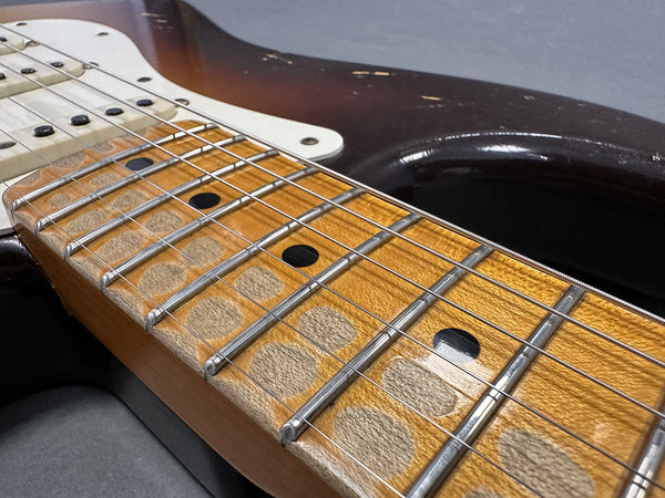 Close-up of vintage electric guitar fretboard with worn maple wood and metal frets, showing strings and dot inlays on a sunburst body background