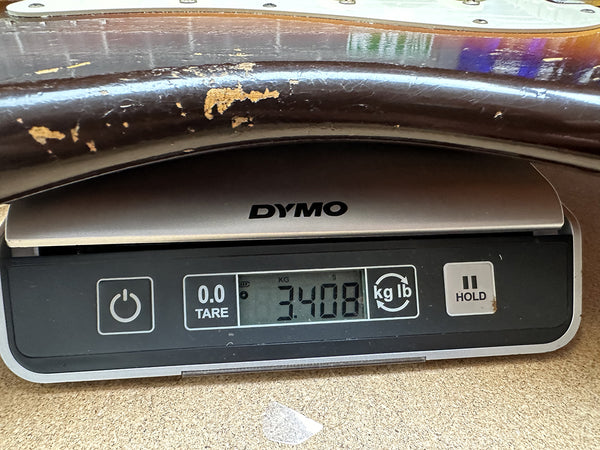 Close-up of a worn electric guitar body placed on a DYMO digital scale showing a weight of 3.408 kilograms, highlighting guitar weight for buyers.