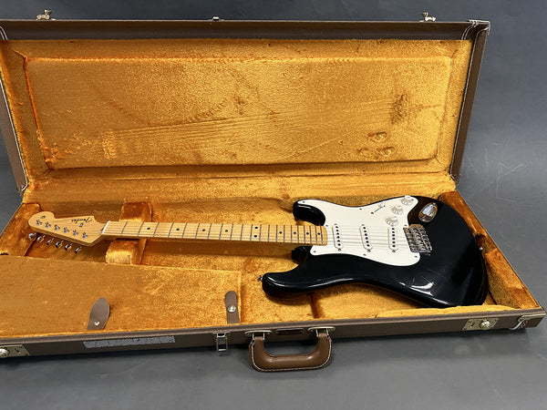 Fender Stratocaster electric guitar with maple neck and black body inside vintage orange-lined hardshell case on gray background