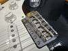 Close-up of black Fender electric guitar bridge, white volume and tone control knobs, and strings on white pickguard with metal saddles marked Fender.