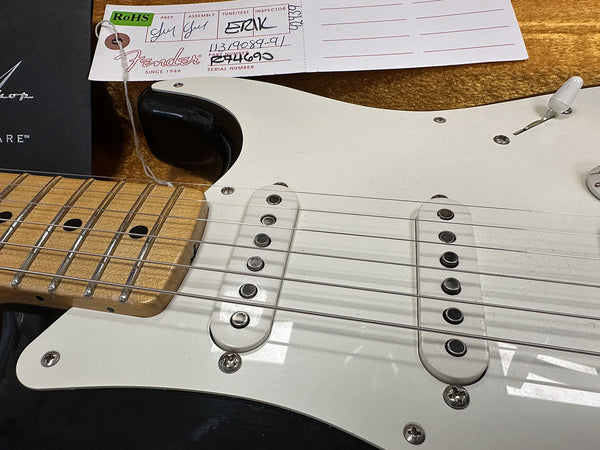 Close-up of Fender Stratocaster electric guitar white pickguard, two single-coil pickups, maple fretboard, and part of Fender quality control tag with serial number and inspector signatures.
