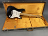 Black Fender Stratocaster electric guitar with maple fretboard and white pickguard in a vintage orange plush-lined hard case