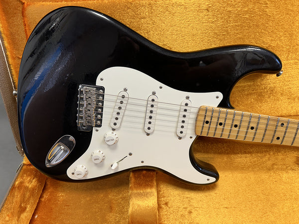 Black electric guitar with white pickguard and three single-coil pickups inside vintage orange guitar case