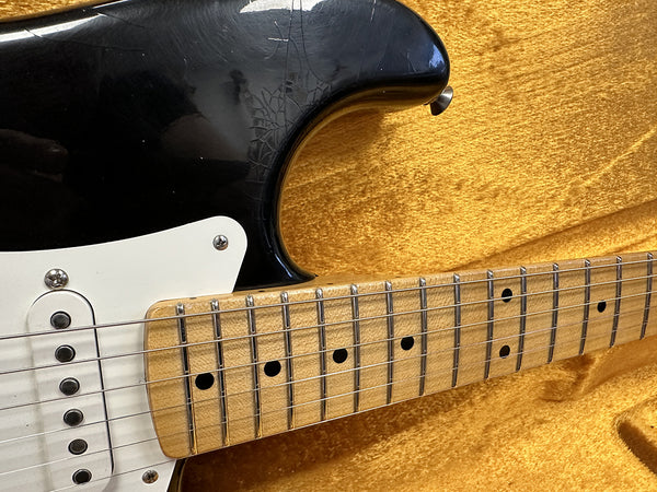 Close-up of black electric guitar body and maple fretboard with dot inlays inside a yellow plush guitar case