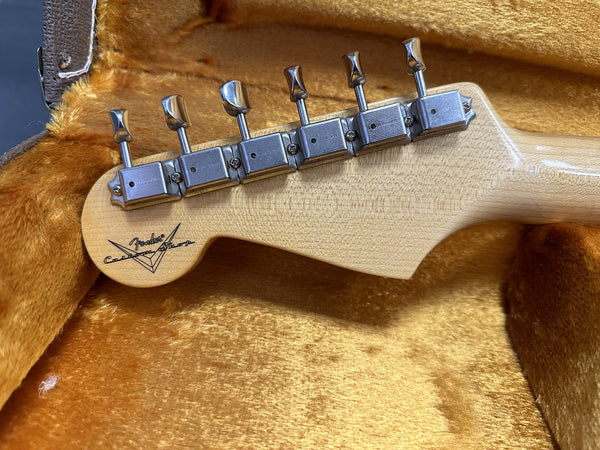 Close-up of vintage Fender Custom Shop guitar headstock with six metal tuning pegs, resting inside a plush gold-lined guitar case