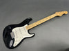 Black Fender Stratocaster electric guitar with maple neck and white pickguard on gray background