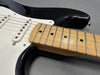 Close-up of black electric guitar body with white pickguard and maple neck fingerboard showing frets and pickups