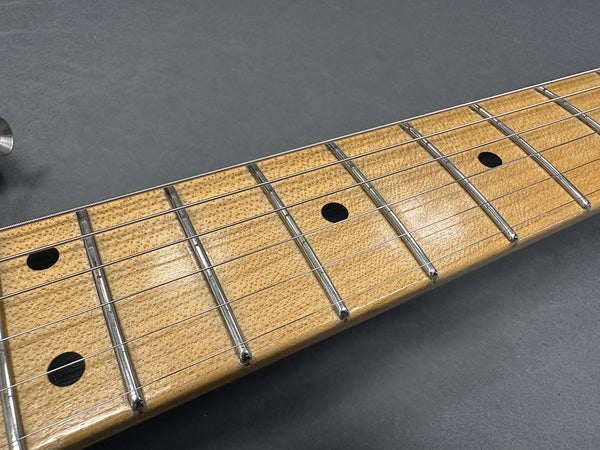 Close-up of maple guitar neck and fretboard with metal frets and black dot inlays on a grey background