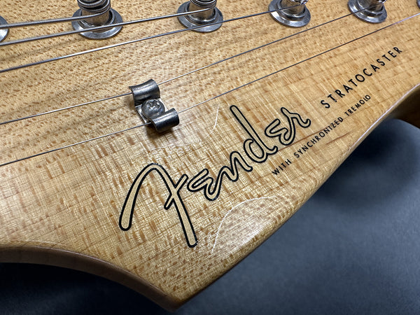 Close-up of natural wood Fender Stratocaster guitar headstock with tuning pegs and synchronized tremolo text