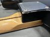 Close-up of guitar neck joint showing maple neck with skunk stripe and black guitar body with metal neck plate and visible wear and finish checking