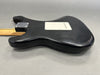 Black electric guitar body with white backplate and natural wood neck on gray background, showing worn finish and scratches