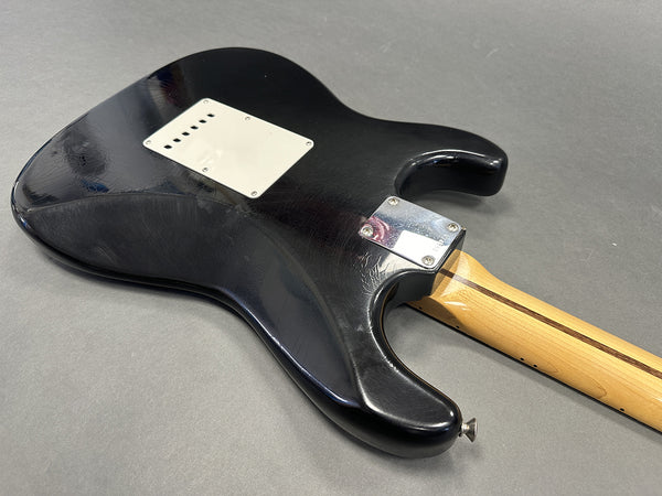 Black electric guitar back body with chrome neck plate and maple neck on gray background