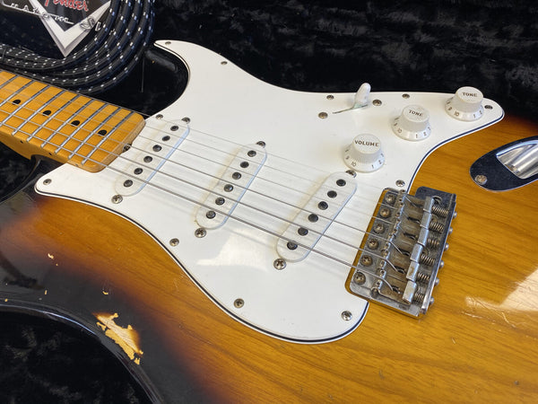 Close-up of vintage sunburst Fender Stratocaster electric guitar body showing pickups, pickguard, volume and tone controls, and worn finish details